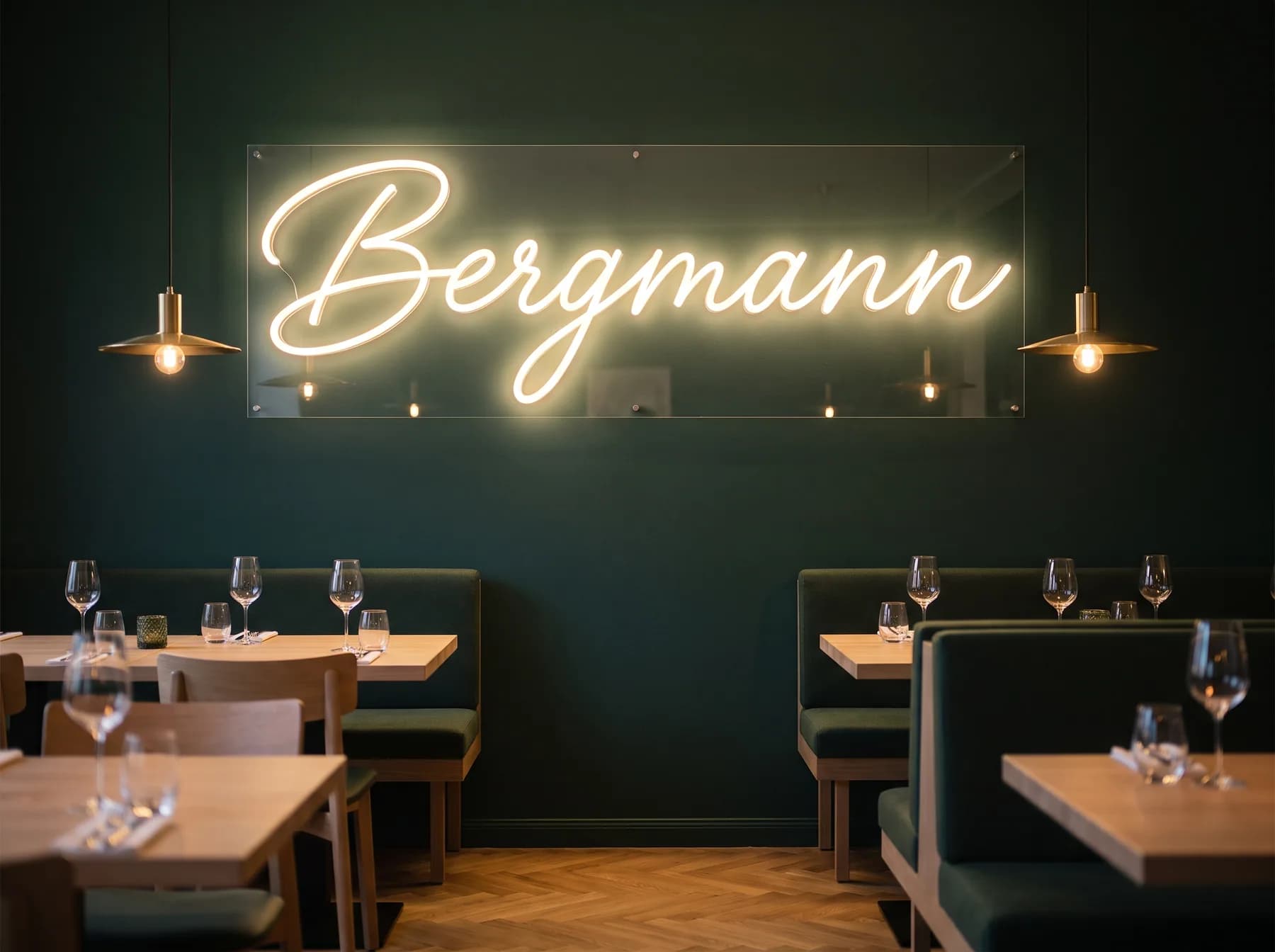 Großformatiger warmweißer Neon-Schriftzug in Schreibschrift auf einer dunkelgrünen Wand im Gastraum eines Restaurants
