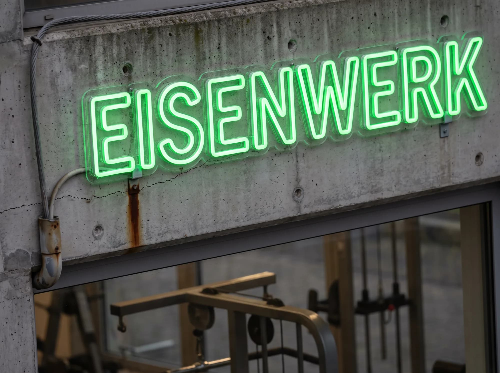 Green outline neon lettering on the concrete lintel of a gym
