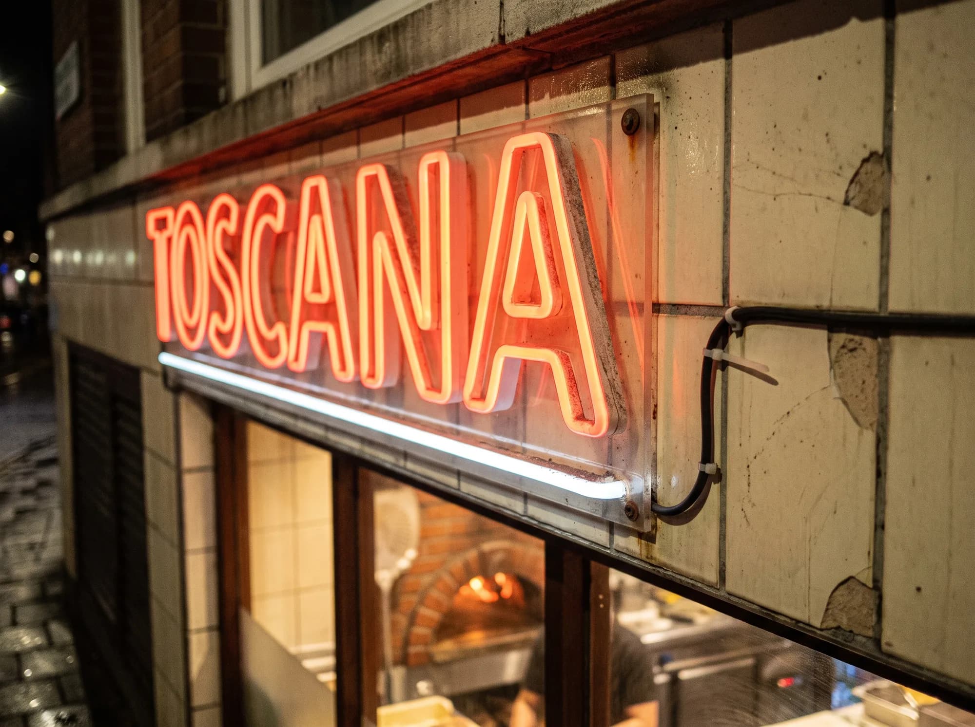 Red neon lettering with a white underline on the tiled fascia of a pizzeria at night
