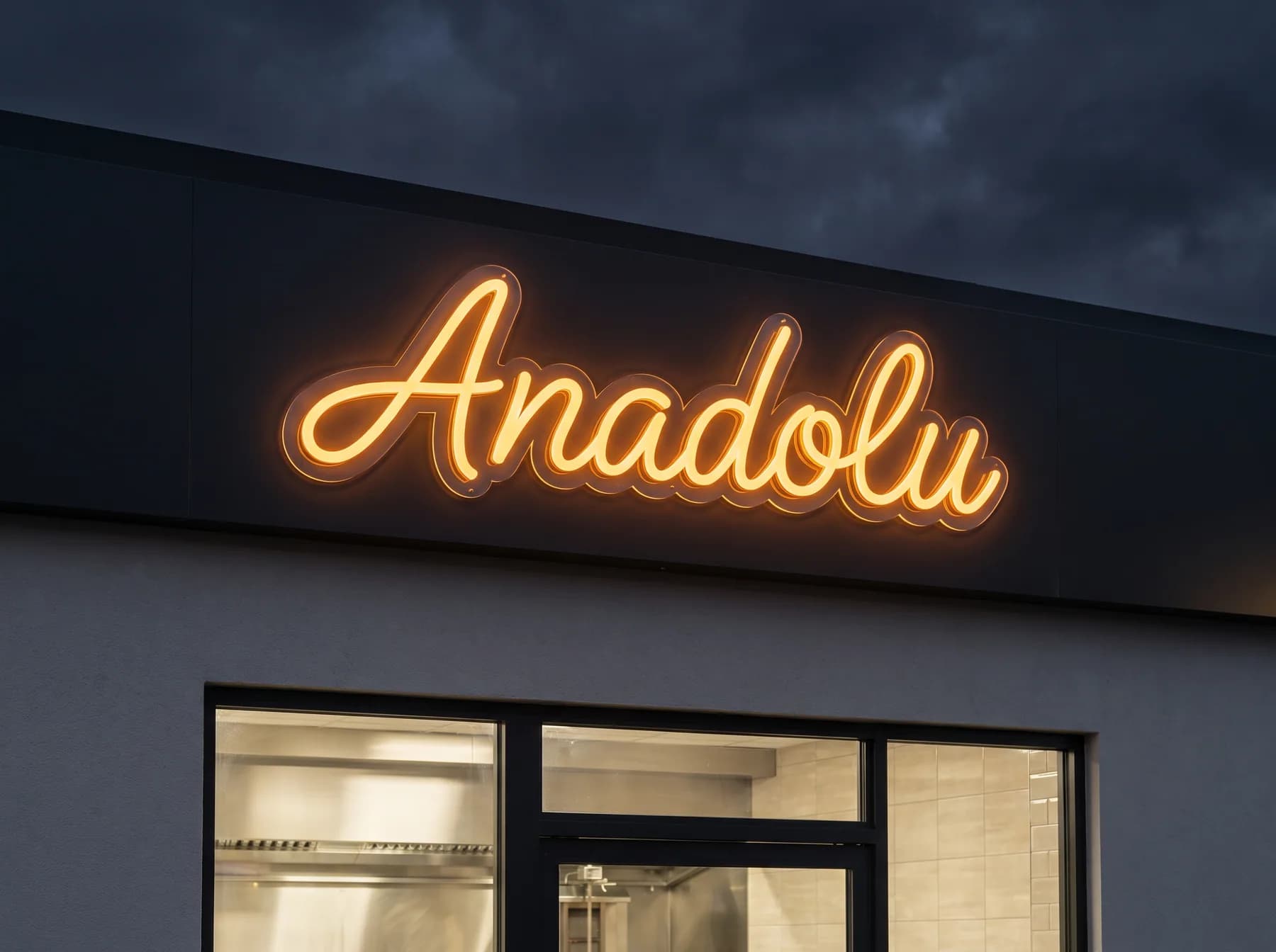 Bernsteinfarbener Neon-Schriftzug in Schreibschrift auf der anthrazitfarbenen Fassadenblende eines Imbisses bei Nacht