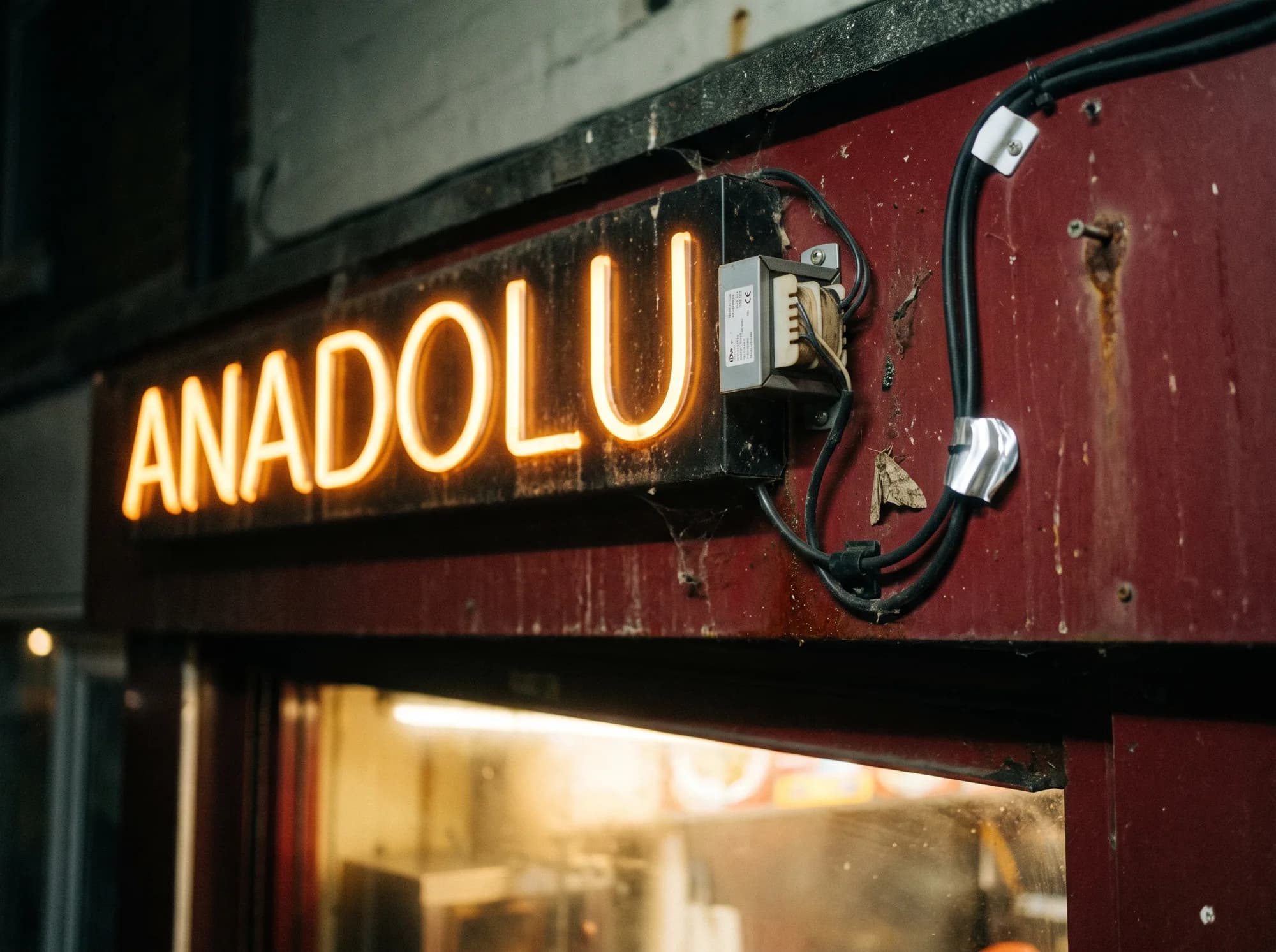 Amber neon lettering on the fascia of a kebab takeaway, with the power supply and cable run beside it